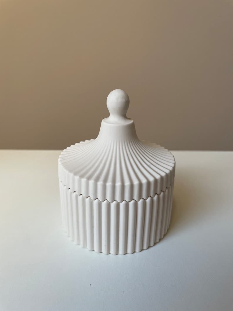 decorative candle set with a flower-shaped candle and an elegant ribbed container with lid, placed on a tray